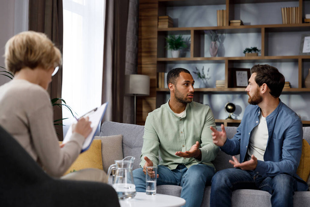 Family quarrel at the reception at the psychologist. LGBT couple at a psychotherapists appointment. Psychologist for gays. Support for the LGBT community in visiting a psychologist - Photo, image