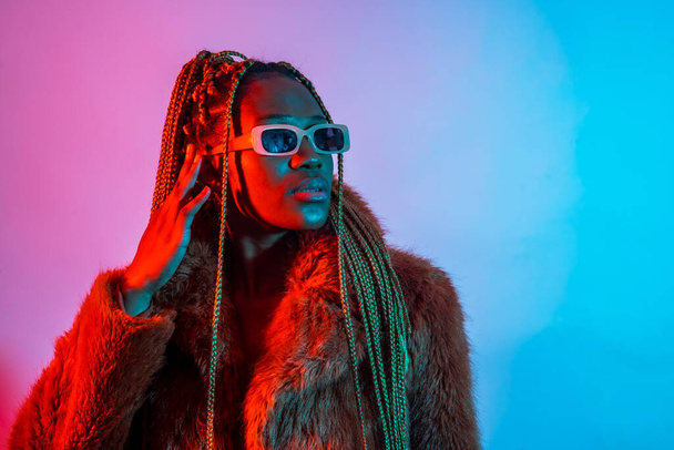 Black ethnic woman with braids with red and blue led lights, studio shoot with sunglasses - Фото, зображення