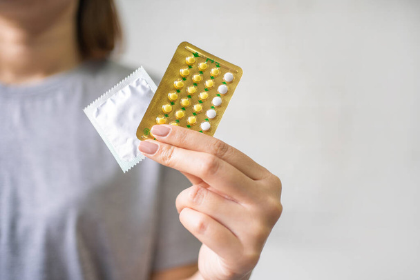 Ontraceptive significa: Donna mano tenendo pillole contraccettive e preservativo. Protezione, sesso sicuro. Contraccezione, concetto di contraccezione.  - Foto, immagini