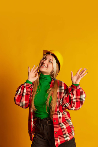 Retro style portrait of young happy blond girl in vintage style clothes in protective helmet isolated on yellow background. Vivid emotions, happiness, hobbies and fashion. Looks delighted, excited - Foto, afbeelding