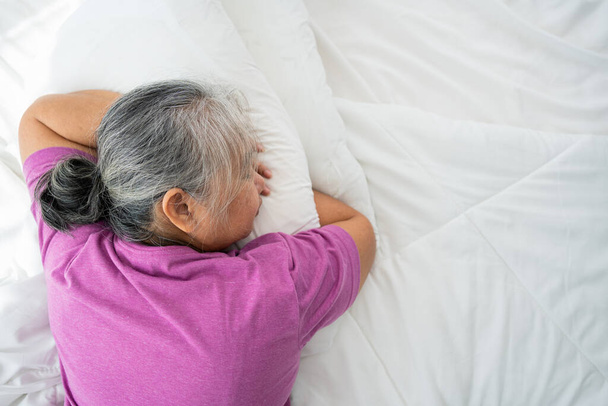 Старшая женщина с седыми волосами в постели чувствуют себя подавленными или страдают от сильной головной боли мигрени и высокого кровяного давления, бессонница пытается спать нарушенный бросок и поворот в спальне - Фото, изображение