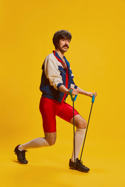 Portrét stylového muže s knírem pózujícího ve veteránském sportovním oblečení, trénink izolovaný přes žluté pozadí. Sportovní životní styl. Koncept retro stylu, kreativity, emocí, výrazu obličeje, módy - Fotografie, Obrázek