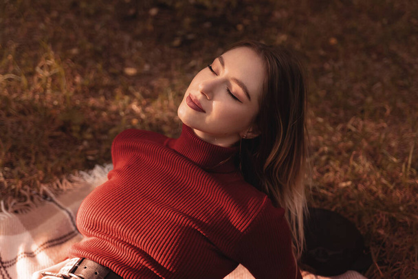 young and beautiful woman in red golf enjoys the sun in the park in autumn - Foto, Imagem