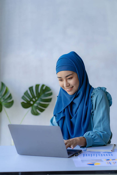 El concepto de gestión impulsa el crecimiento organizacional de las mujeres líderes. Mujer musulmana asiática con hiyab se sienta en la oficina de una empresa de nueva creación. gestionada y dirigida por mujeres jóvenes - Foto, Imagen