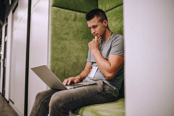 Serieuze gericht Kaukasische jonge mannelijke werknemer gezeten in de introverte werkplek staren naar zijn laptop - Foto, afbeelding