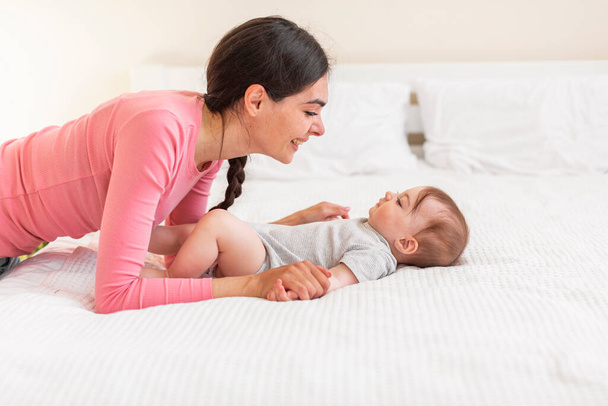 Mother-child connection. Loving mommy bonding with her adorable newborn child at home, relaxing on bed together, side view, copy space - Foto, Bild