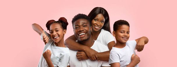 Feliz família afro-americana amorosa jovem marido e mulher e crianças menino e menina adolescentes posando no fundo do estúdio rosa, vestindo camisetas brancas, panorama, colagem. Conceito familiar - Foto, Imagem