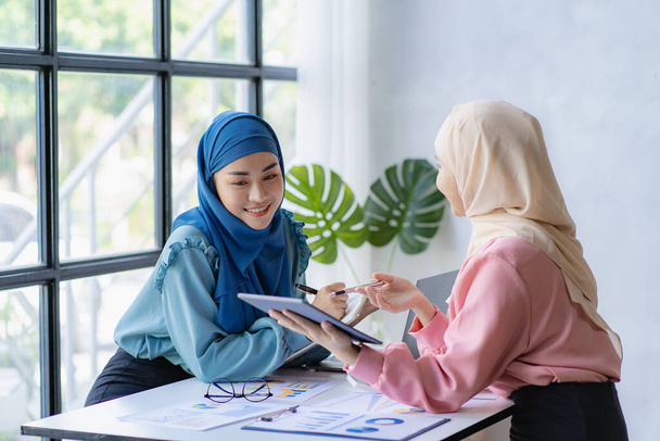 Dos jóvenes musulmanas modernas que trabajan y discuten el trabajo en la reunión de negocios en la sala de reuniones con gráficos financieros y computadora portátil - Foto, imagen