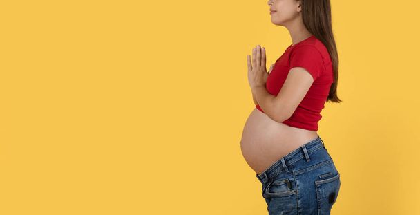 Περικοπή πυροβόλησε έγκυος γυναίκα στέκεται με σφιγμένα χέρια πάνω από το κίτρινο φόντο, Νεαρή προσδοκώμενη κυρία με μεγάλη κοιλιά προσεύχεται ή ζητώντας συγχώρεση, πλευρική άποψη, Πανόραμα με αντίγραφο χώρο - Φωτογραφία, εικόνα