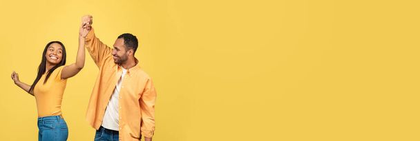 Extended Shot Of Cheerful Black Young Couple Dancing Over Yellow Background, Happy Joyful Romantic African American Spouses Having Fun Together, Holding Hands And Laughing, Wide Horizontal Banner - 写真・画像