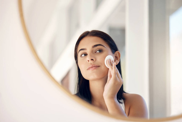Face, beauty and mirror with a woman cleaning her skin in the bathroom of her home in the morning. Skincare, reflection and cosmetics with an attractive young female going through her facial routine. - Foto, Imagen