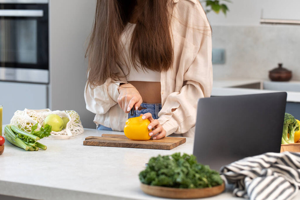 A woman is preparing a vegetable salad in the kitchen in front of a laptop. The concept of a culinary video blog, a blog about healthy eating. - Fotó, kép