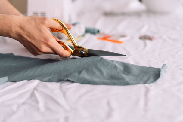 Señora corta con tijeras de un trozo de tela delante de una herramienta de coser. - Foto, imagen