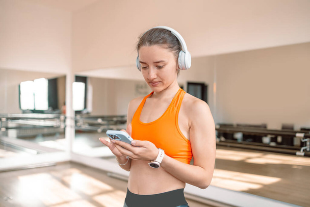 Активная молодая кавказская спортсменка-тренер по спортивной фитнесу инструктор женщина, пользующаяся смартфоном, слушающая музыку в тренажерном зале. Спортивная концепция.  - Фото, изображение