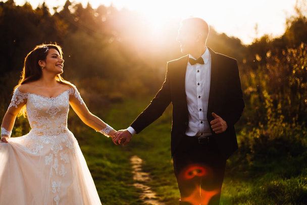 Жених и невеста в день свадьбы гуляют на природе. Молодожены держатся за руки и ходят. вечер - Фото, изображение