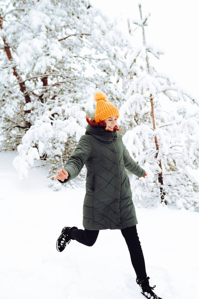 Vidám lány vörös haj meleg ruhákban játszik hó a szabadban, közel a gyönyörű erdő - Fotó, kép