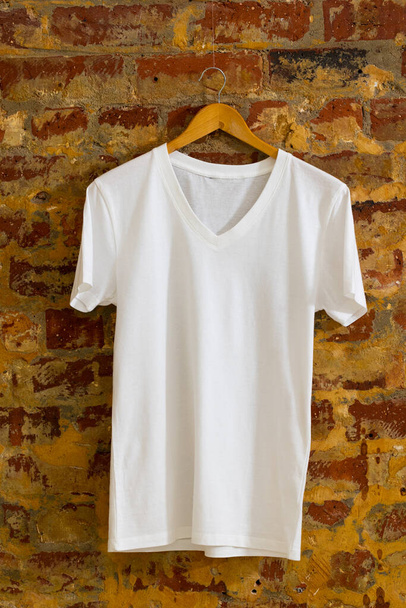 Tshirt hanging on coat hanger and copy space on brick background. Clothing, fashion and retail concept. - 写真・画像