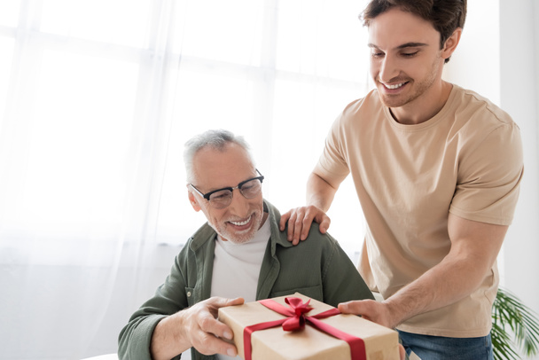 mladý muž dává dárkové krabice na šťastný táta, zatímco gratuluje mu na otců den - Fotografie, Obrázek