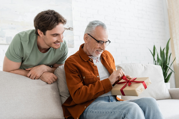 young man smiling near pleased dad opening present on fathers day - Photo, Image