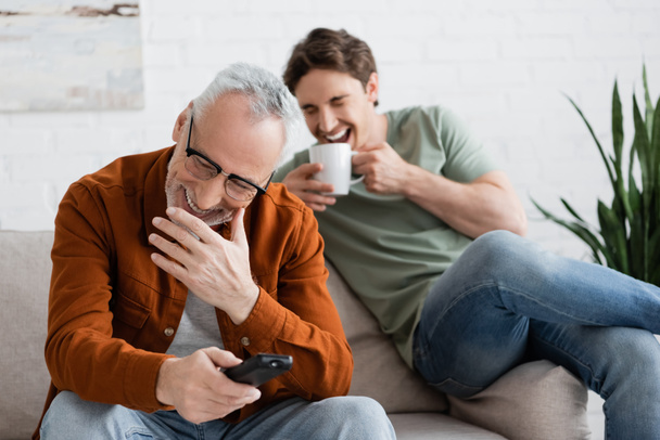 excited father and son watching comedy movie and laughing in living room - Photo, Image