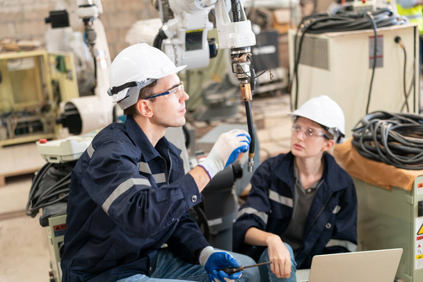 Ingénieurs en robotique travaillant sur la maintenance d'un bras robotique moderne dans un entrepôt d'usine - Photo, image