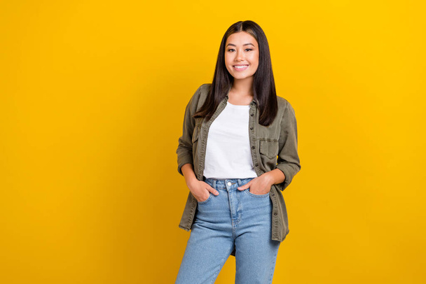 Portrait of cheerful pleasant sweet girl long hairstyle dressed khaki shirt standing arms in pockets isolated on yellow color background. - Foto, Imagem