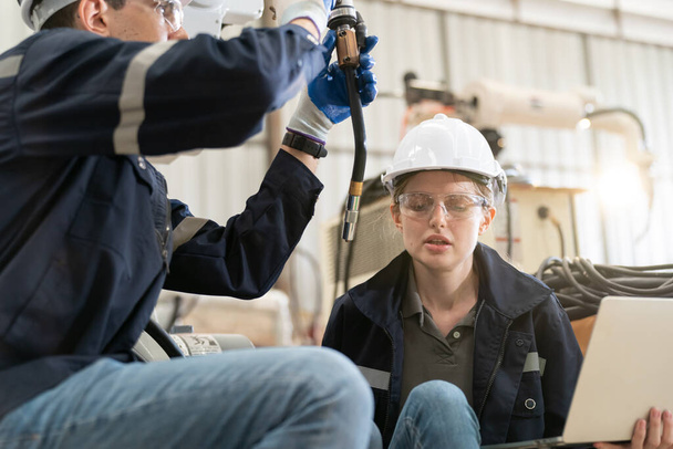 Ingénieurs en robotique travaillant sur la maintenance d'un bras robotique moderne dans un entrepôt d'usine - Photo, image