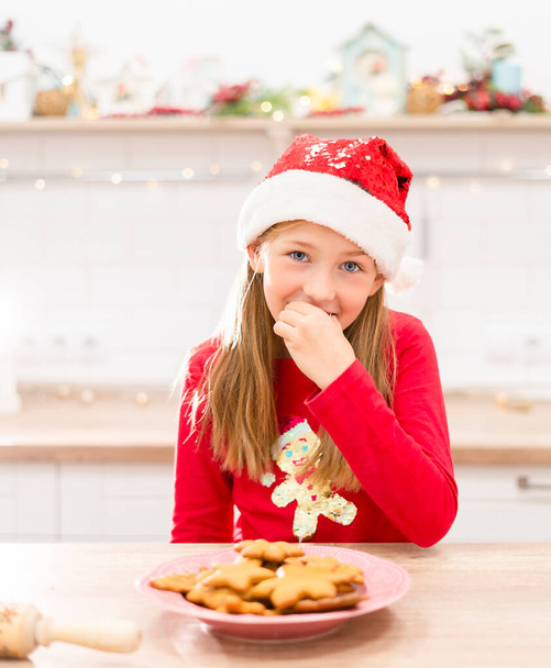 Fiatal boldog tini lány ül a konyhában karácsonyi hangulat és eszik mézeskalács karácsonyi sütik - Fotó, kép