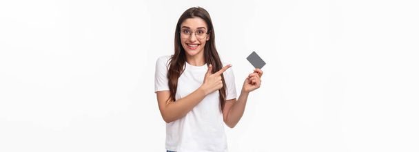 Porträt einer aufgeregten, glücklichen jungen Frau, die über ihre Bank spricht, auf Kreditkarte zeigt und lächelnd in die Kamera lächelt, Ratschläge für bargeldloses Bezahlen, Online-Kauf von Waren, weißer Hintergrund. - Foto, Bild
