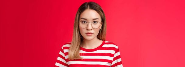 Yakın çekim odaklı zeki Asyalı kız öğrenci dikkatle dinle konferans kameraya odaklan gözlük tak çizgili tişört giy kırmızı arka plan. Boşluğu kopyala - Fotoğraf, Görsel