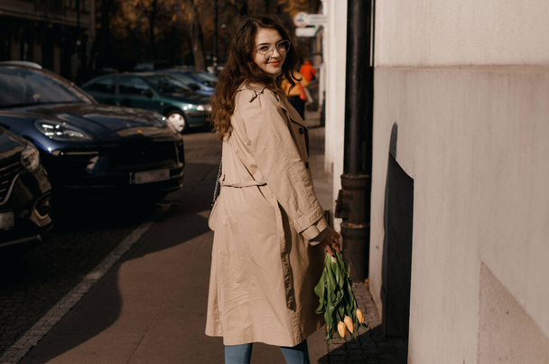 Νεαρή γυναίκα με παλτό έξω. Εξωτερική φθινόπωρο πορτρέτο της νεαρής κομψής μόδας γυναίκα φορώντας μοντέρνα γυαλιά, καμήλα χρώμα παλτό, τσάντα ώμου, το περπάτημα στο δρόμο της ευρωπαϊκής πόλης. Αντιγραφή χώρου - Φωτογραφία, εικόνα