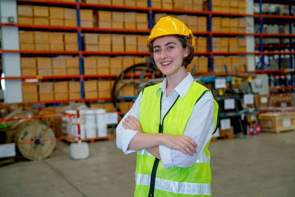 Portrait of Caucasian warehouse factory worker woman with arm crossed and look at camera also stay in workplace with the layer of boxes on shelves in the background. - Foto, imagen