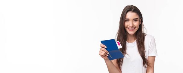 Travelling, holidays, summer concept. Close-up portrait beautiful young woman with long hair, traveller sitting in airport, holding passport and airplane ticket, going for vacation, white background. - Valokuva, kuva