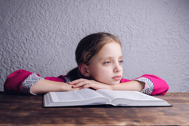 A European American girl is reading a book. An open Bible on the table. - Photo, Image