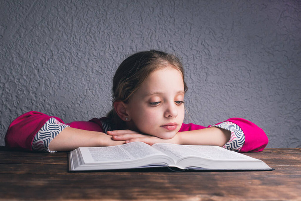 Ein europäisch-amerikanisches Mädchen liest ein Buch. Eine offene Bibel auf dem Tisch. - Foto, Bild