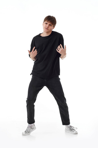 young man in black t-shirt and jeans dancing on white background. Full length - Foto, Imagem