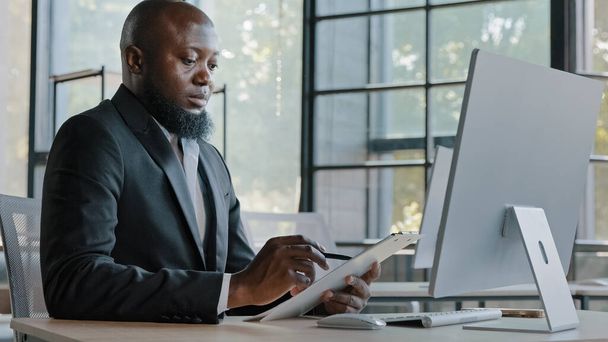 Αφρικανός συγγραφέας γράφει σημειώσεις σε χάρτινη ταμπλέτα κάθονται στο γραφείο ενηλίκων επιχειρηματίας Αμερικανός επιχειρηματίας δημιουργούν νέες ιδέες εταιρικά καθήκοντα επιχειρηματική στρατηγική σχέδιο μάρκετινγκ συμπληρώστε τα σημεία στη λίστα ελέγχου - Φωτογραφία, εικόνα