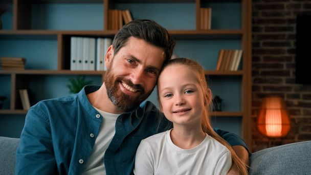 Happy Caucasian family diverse generation people beautiful daughter and father sit on sofa posing together at home daddy hug beloved little child girl kid harmony bonding embrace childcare fatherhood - Photo, Image