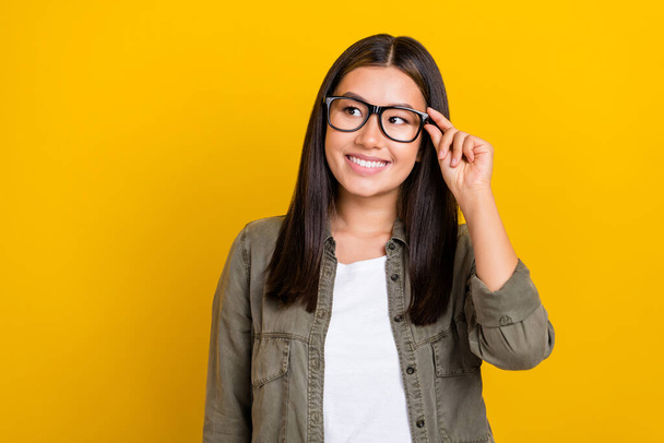 Portrait of gorgeous clever woman with long hairdo wear khaki shirt look empty space touch glasses isolated on yellow color background. - Photo, image