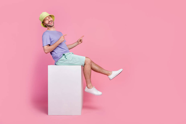 Full size photo of handsome young guy sit shopping billboard direct empty space dressed trendy blue look isolated on pink color background. - Foto, afbeelding