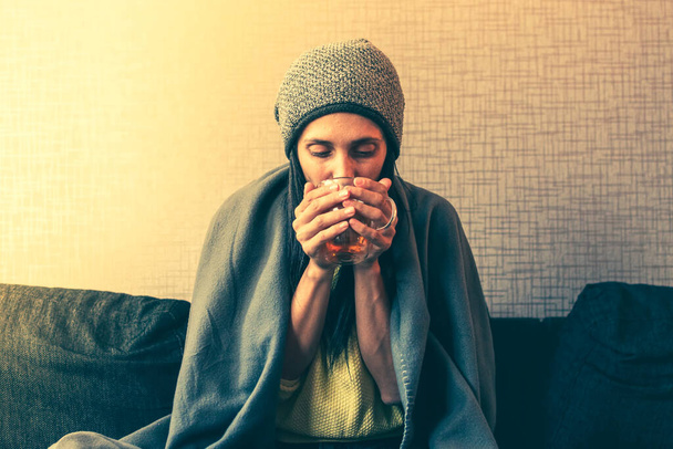 白人心配している悲しい女性は、紅茶を飲みながらソファの上に毛布の下に座っています,インフレと戦争のためにガス法案のための民間世帯の上昇コスト,エネルギー危機 - 写真・画像