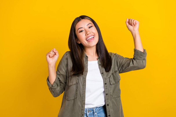 Portrait of nice adorable cheerful girl long hairdo wear khaki shirt raise fists up shout yell yes isolated on yellow color background. - Foto, Imagen