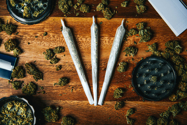 Marihuana scholen op een houten tafel. Slijpmachine, filterpapier en sigaretten. Drugs op een tafel achtergrond met cbd of thc, indica of sativa knoppen. - Foto, afbeelding