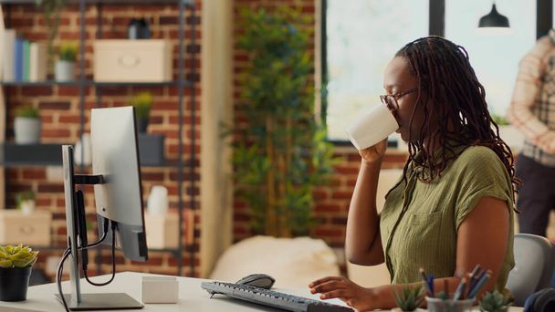 Afrykański amerykański pracownik pracujący w domu, wykonujący zadania księgowe i sprawdzający raporty online. Przeglądanie danych internetowych i wysyłanie e-maili do menedżera, sieci marketingowej. - Zdjęcie, obraz