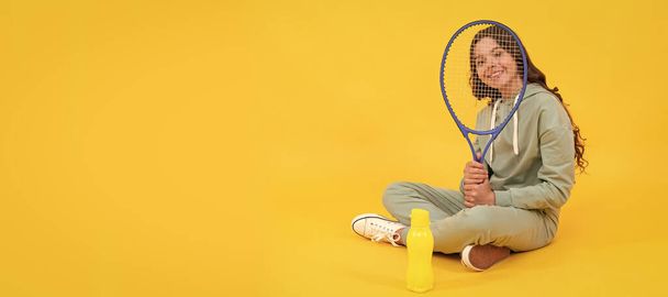 boldog gyermek ül sportruházatban squash ütő és vizes palack sárga alapon. Vízszintes plakát elszigetelt gyermek arc, banner fejléc, másolás tér - Fotó, kép
