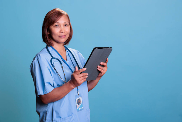 Азійська медсестра, яка тримає планшет, перевіряє медичний рецепт, перш ніж розпочати огляд відвідувань хворого пацієнта. Лікар-асистент у синій формі працює в галузі охорони здоров'я, медична концепція - Фото, зображення
