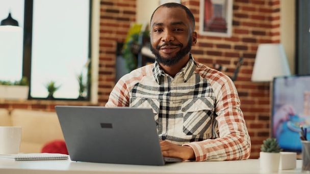 Afroamerikaner, der fernab von zu Hause arbeitet, Laptop benutzt und Geschäftsberichte über das Vertriebsnetz schreibt. Männliche Freiberufler lernen online in der Wohnung, Buchhaltung Ausbildung. Handschuss. - Foto, Bild