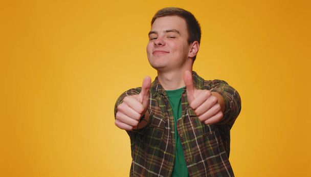 Like. Teenager adult man in green shirt raises thumbs up agrees with something or gives positive reply recommends advertisement likes good. Young guy boy isolated alone on yellow studio background - Photo, Image