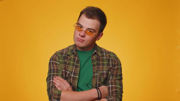 Playful happy teenager adult man 20 years old wearing yellow sunglasses blinking eye looking at camera with toothy smile, winking and flirting expressing optimism. Young guy boy on yellow background - Foto, immagini