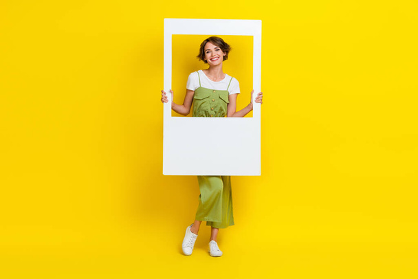 Full length photo of cute young lady toothy smile hold white instant photo frame dressed trendy khaki clothes isolated on yellow color background. - Φωτογραφία, εικόνα